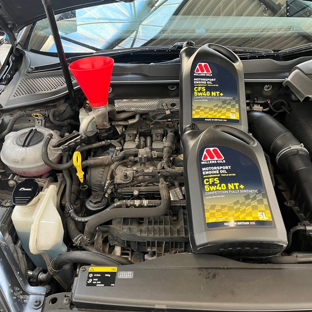 Engine bay with a funnel and two 5 litre cans of Millers CFS 5w40 oil ready for an oil change